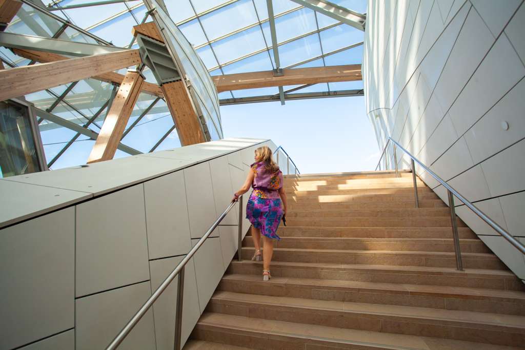 Sarah walking up a wooden staircase under a glass roof in Paris
