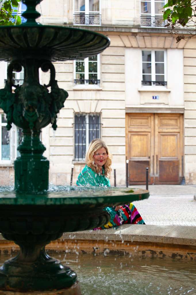 Sarah sitting by a Paris fountain in a striped dress